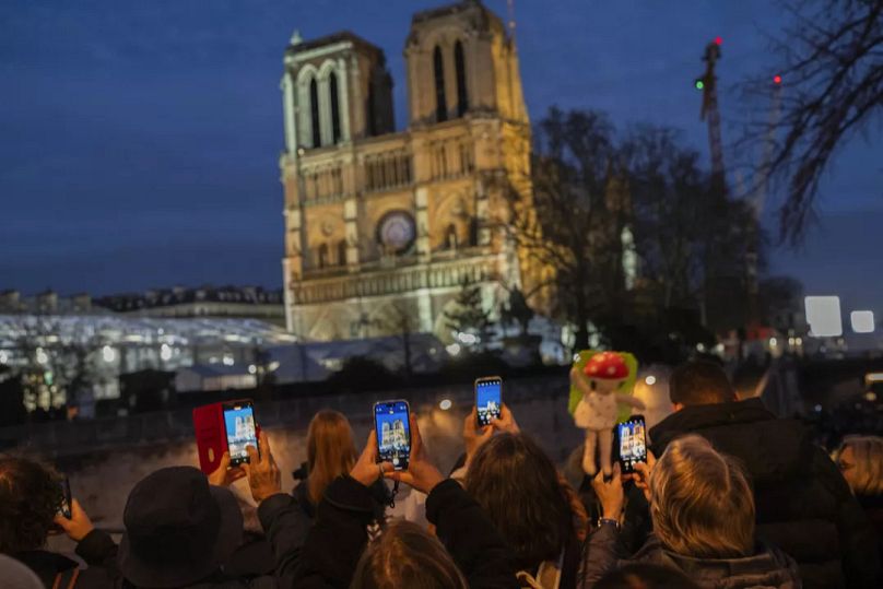 Fußgänger machen Schnappschüsse von der Kathedrale Notre Dame einen Tag vor ihrer feierlichen Wiedereröffnung in Paris am Freitag, 6. Dezember 2024.