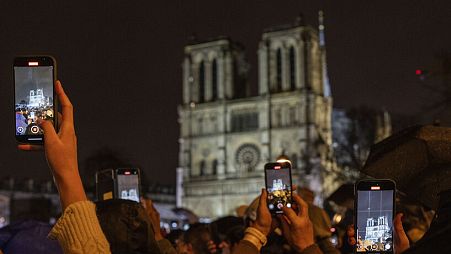 Spectators take snapshots outside France's iconic Notre Dame Cathedral Saturday, Dec. 7, 2024 in Paris during it's formal reopening for the first time since a devastating fire