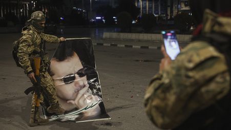 Боец сирийской оппозиции фотографирует товарища, наступившего на портрет президента Сирии Башара Асада в Алеппо, 30 ноября 2024 года