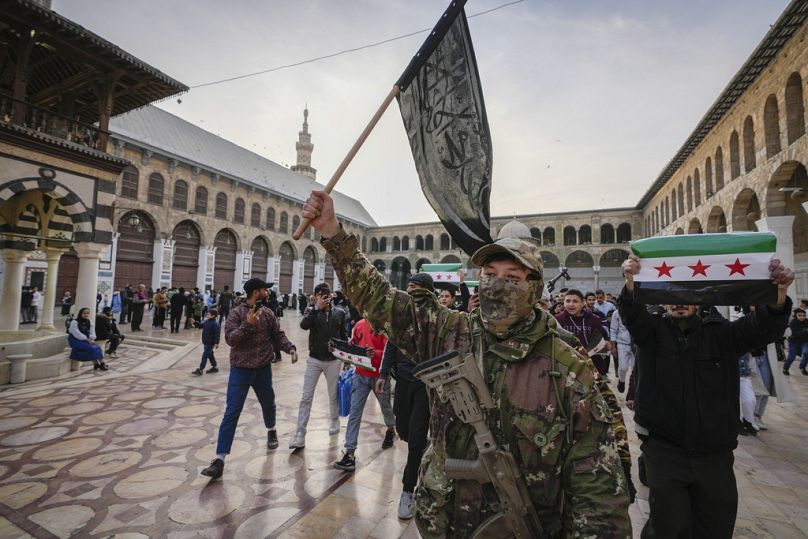 Ein maskierter Oppositionskämpfer trägt in Damaskus eine Fahne von Hayat Tahrir al-Sham (HTS), 10. Dezember 2024.