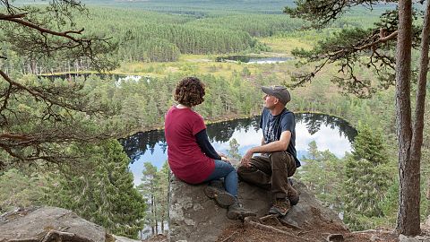 A couple sit and look out across Uath Lochans in Cairngorms National Park, Scotland 