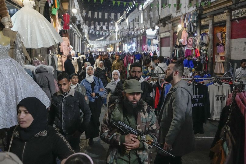 Un combattant de l'opposition armée se promène parmi les clients du marché Al-Hamidiyeh dans la vieille ville fortifiée de Damas, en Syrie, le mardi 10 décembre 2024.