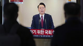 People watch a TV screen showing the live broadcast of South Korean President Yoon Suk Yeol's announcement at the Seoul Railway Station in Seoul, South Korea, Thursday, Dec. 1