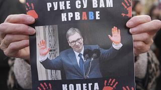 Una donna regge un cartello con il presidente serbo Aleksandar Vučić e la scritta "Hai le mani sporche di sangue!".