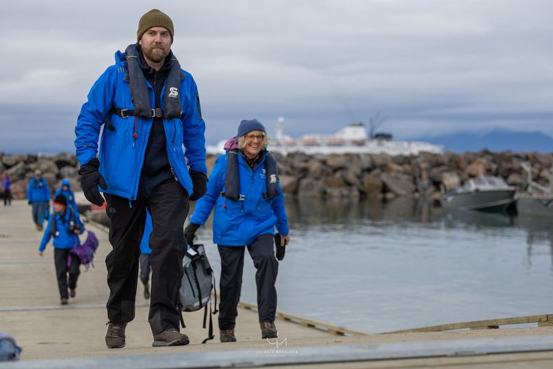 Nick Dauk e altri passeggeri camminano con indosso le giacche blu e i salvagenti