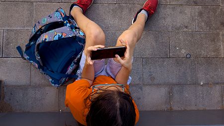An 11-year-old boy plays with his father's phone outside school in Barcelona, Spain, Monday, June 17, 2024.