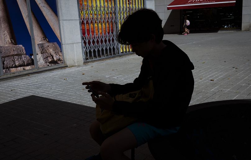 A 12-year-old boy plays with his personal phone outside school in Barcelona, Spain in June 2024.