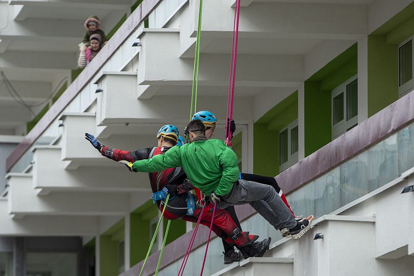 Kosovo alpinists disguised as superheroes wave at children as they descend with ropes from the hospital roof offering gifts to children in Pristina, 13 December, 2024