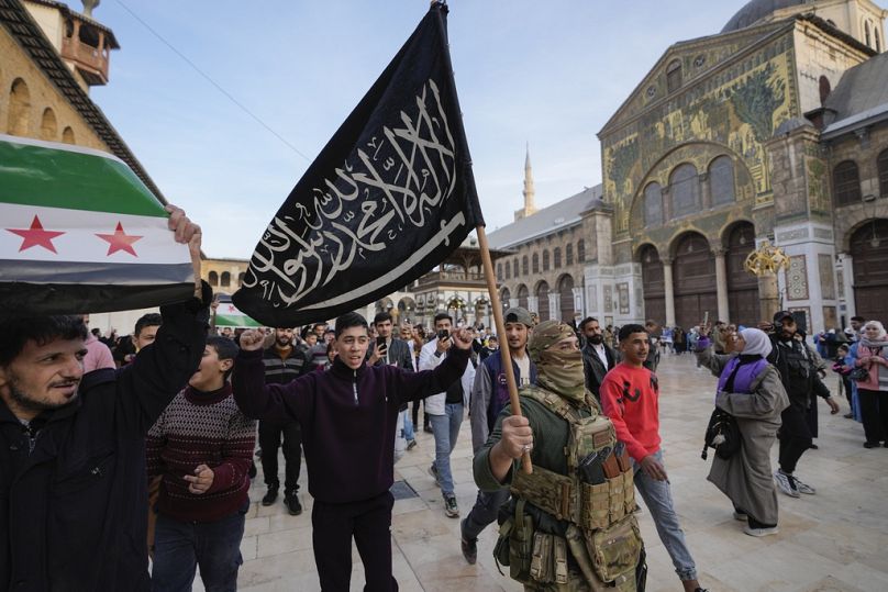  معارض ملثم يحمل علم هيئة تحرير الشام في باحة المسجد الأموي في مدينة دمشق القديمة، سوريا، يوم الثلاثاء، 10 ديسمبر 2024. 