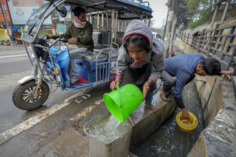 Persone raccolgono acqua da un tombino aperto a Guwahati, India