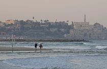 Una coppia passeggia lungo la riva di una spiaggia di Tel Aviv, in Israele.