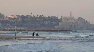 A couple walks along the shore of a beach in Tel Aviv, Israel.