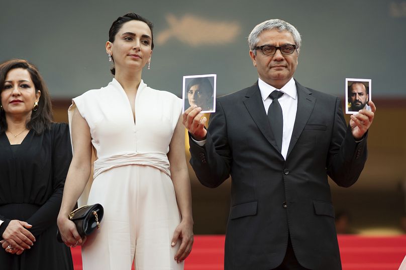 Director Mohammad Rasoulof, right, holds photographs of actors Missagh Zareh, left, and Soheila Golestani, besides Mahsa Rostami - Cannes 2024