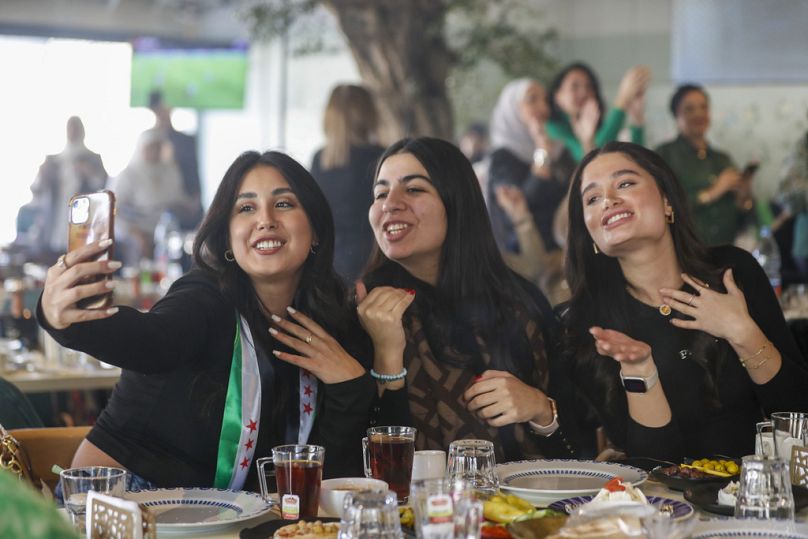 A Syrian woman with a scarf in colors of "revolutionary" Syrian flag takes a selfie with her friends as they celebrate in a restaurant in Damascus, Syria, Tuesday, Dec. 17