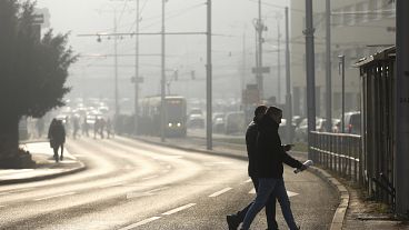 Persone attraversano la strada avvolte dalla foschia dell'inquinamento mentre lo smog ricopre Sarajevo, in Bosnia, nel dicembre 2024.