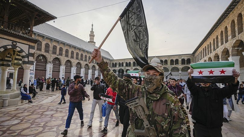 A masked opposition fighter carries a flag of Hayat Tahrir al-Sham (HTS) in the courtyard of the Umayyad Mosque in the city of Damascus, Syria, on Tuesday, Dec. 10, 2024.