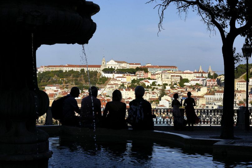 Persone sedute sul bordo di una fontana si godono la vista del centro di Lisbona da una delle colline della capitale portoghese, 15 settembre 2024