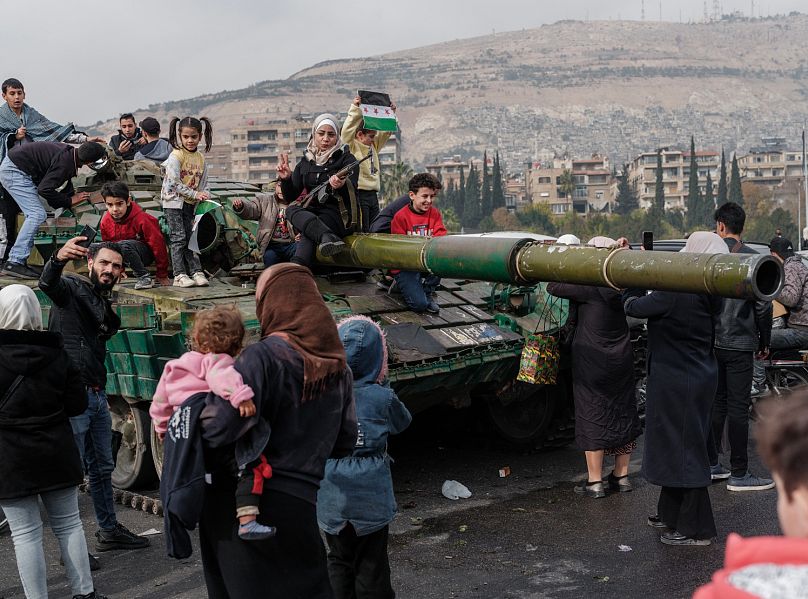 Ciudadanos sirios celebran en lo alto de un tanque gubernamental abandonado en Damasco, Siria