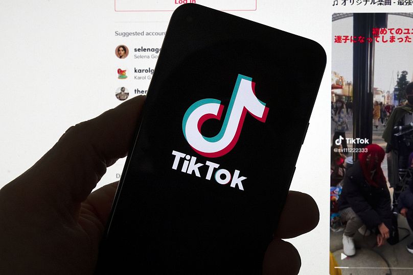 The TikTok logo is displayed on a mobile phone in front of a computer screen which displays a TikTok home page in Boston, 18 March, 2023