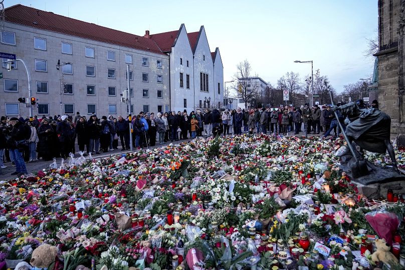 Des gens déposent des fleurs et allument des bougies devant l'église Saint-Jean près du marché de Noël de Magdebourg, en Allemagne, le dimanche 22 décembre 2024.