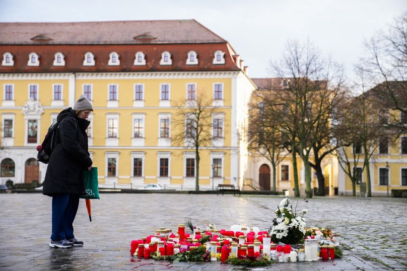 A woman stands next to flowers and candles laid down near the Magdeburg Cathedral, after a car drove into a crowd of a Christmas Mark on Friday evening, in Magdeburg, Germany,