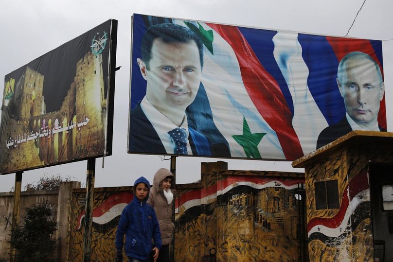 Syrians walk by posters of Syrian President Bashar Assad and Russian President Vladimir Putin in Aleppo, Syria, Thursday, Jan. 18, 2018.