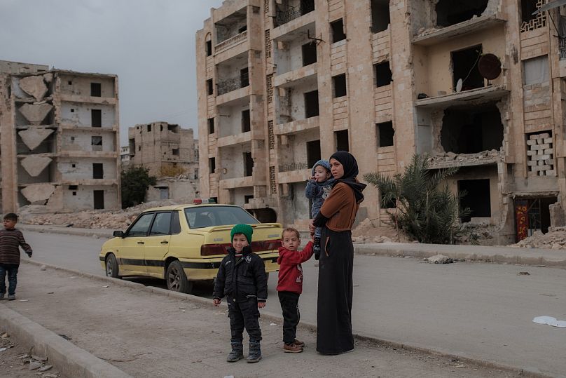 Una madre e i suoi figli in piedi in una strada di Aleppo, in Siria, sullo sfondo di edifici distrutti dalla guerra