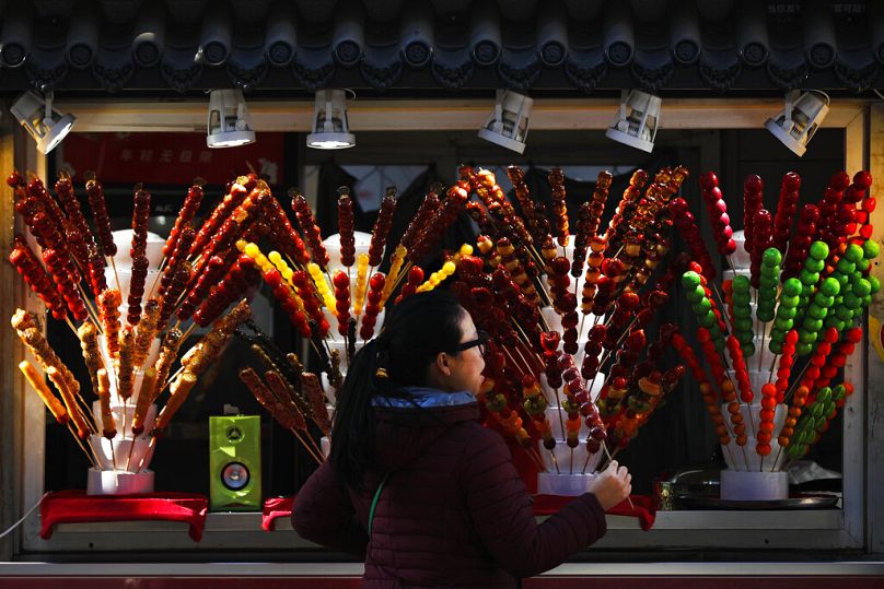 A woman buys a sugar-coated haws, also known as tanghulu, on a stick at a street vendor in Beijing.