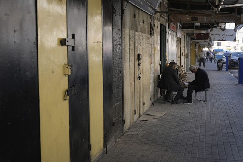فلسطينيون يجلسون أمام محلات تجارية مغلقة خلال إضراب عام دعت إليه قوات الأمن الفلسطينية أثناء حملتها ضد المسلحين في مخيم جنين للاجئين، الاثنين 23 ديسمبر/كانون الأول 2024.