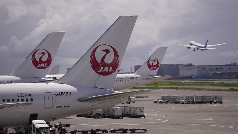 Japan Airlines aircraft are parked at a terminal as another takes off from the Haneda international airport in Tokyo