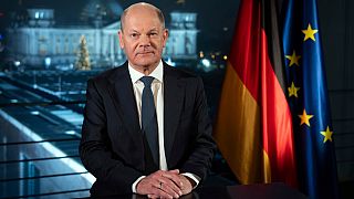 German Chancellor Olaf Scholz sits in front of the backdrop of the Reichstag illuminated by spotlights during a photo session after the recording of his New Year's address.
