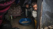 Brothers Belal, 5, and Mohammed Hamad, 7, collect water from their flooded family tent after overnight rainfall at the refugee tent camp, 31 December 2024 