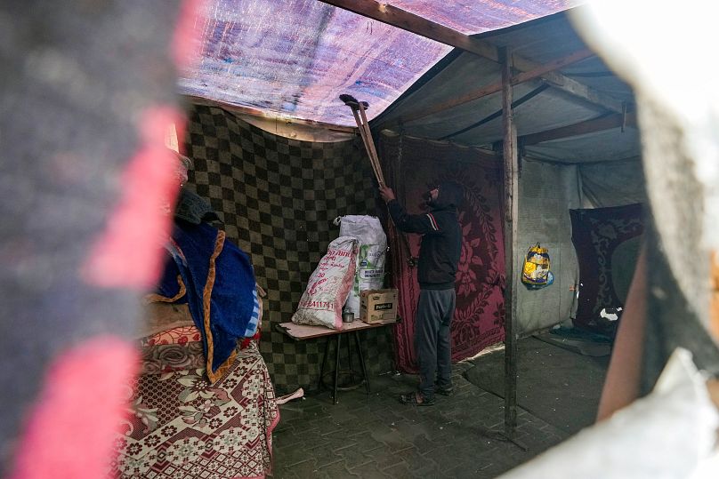 رجل يزيل المياه من السقف القماشي لخيمة مؤقتة بعد هطول الأمطار في دير البلح وسط قطاع غزة، الثلاثاء 31 ديسمبر/كانون الأول 2024