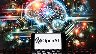 The OpenAI logo is displayed on a cell phone with an image on a computer screen generated by ChatGPT's Dall-E text-to-image model, Dec. 8, 2023, in Boston