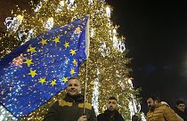 A man with an EU flag stands next to a Christmas Tree in a street decorated for Christmas and the New Year festivities outside of the Georgian arliament, in Tbilisi