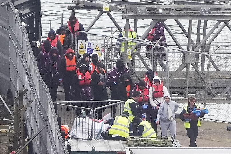 رضيع صغير تحمله امرأة بينما يتم نقل مجموعة من الأشخاص الذين يُعتقد أنهم مهاجرون إلى دوفر، إنجلترا، الأحد، 29 ديسمبر 2024
