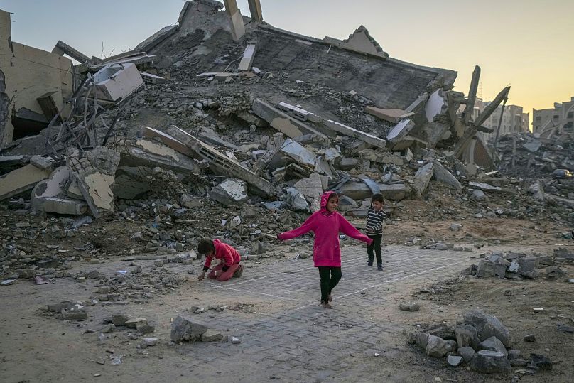 أطفال فلسطينيون يلعبون بجوار مبنى دمرته غارات الجيش الإسرائيلي في بلدة خان يونس وسط قطاع غزة، الأربعاء، 1 يناير/كانون الثاني 2025