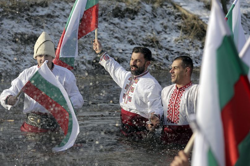 Ciudadanos búlgaros cantan y bailan mientras sostienen banderas en el río Lesnovska, durante las celebraciones del Día de la Epifanía en la ciudad de Elin Pelin, Bulgaria.