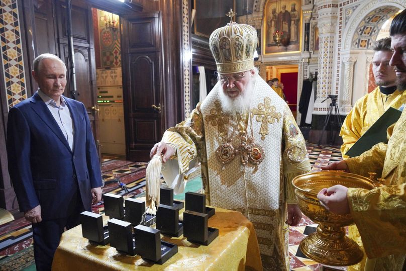 El Patriarca ortodoxo ruso Cirilo , en el centro, acompañado por el presidente ruso Vladimir Putin, a la izquierda, santifica los collares con cruces para los militares rusos
