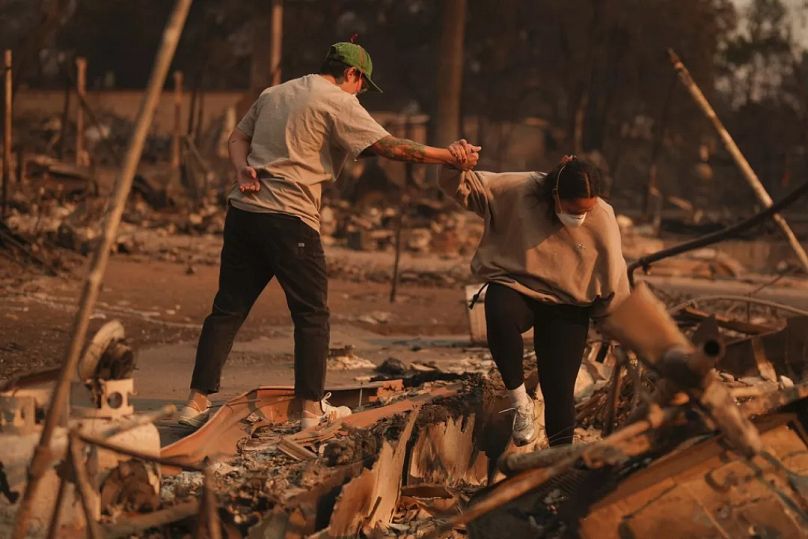 Zwei Menschen stützen sich gegenseitig, als sie ein vom Feuer verwüstetes Grundstück nach dem Eaton-Brand am Donnerstag, 9. Januar 2025, durchwühlen.