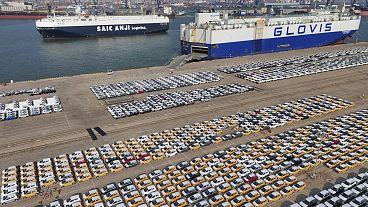Veicoli e camion per l'esportazione attendono di essere trasportati da un porto di Yantai, nella provincia orientale cinese dello Shandong