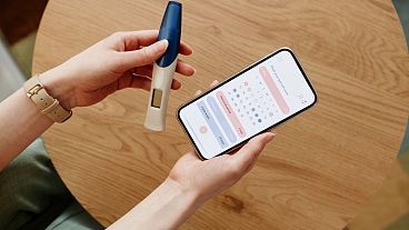 A woman uses an app to calculate her menstrual cycle while holding a pregnancy test.