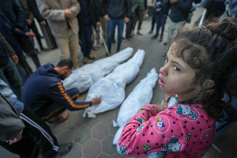 طفلة تشاهد محمد عيد وهو يشيع ابن عمه مع عمها وجدها وقد قُتلوا في غارة جوية إسرائيلية يوم السبت، خلال جنازتهم في دير البلح، وسط قطاع غزة، الأحد، 12 يناير/كانون الثاني 2025