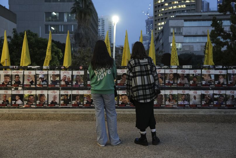 Zwei Frauen betrachten Fotos von im Gazastreifen festgehaltenen Geiseln, die an einem Zaun in Tel Aviv, Israel, angebracht sind am Mittwoch, 15. Januar 2025.