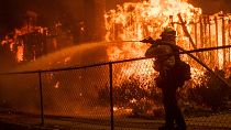 A firefighter sprays water on a home burning in the Eaton Fire in Altadena.