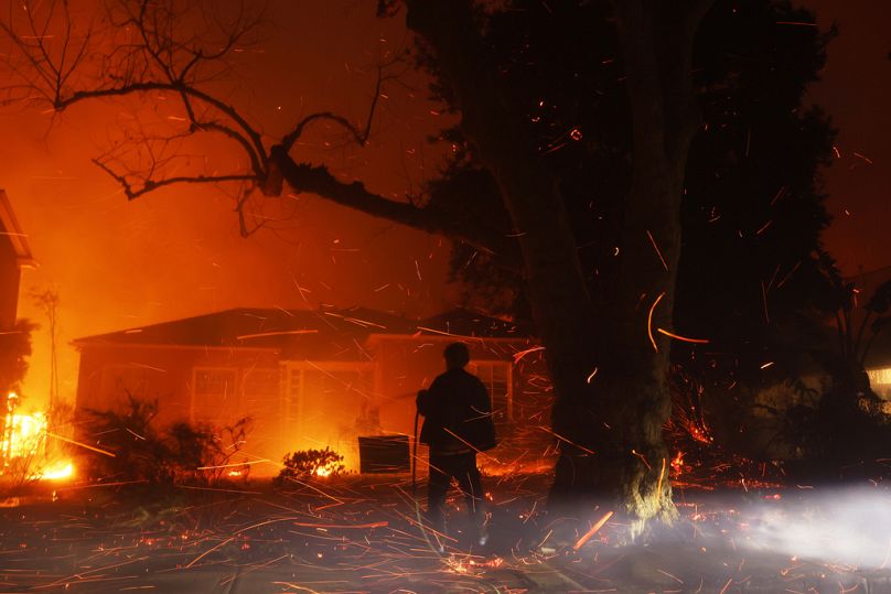 A person tries to hose down embers from the Palisades Fire.