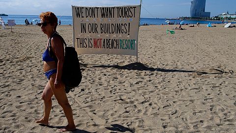 A woman walks past a banner during a protest against tourism in Barcelona, Spain.