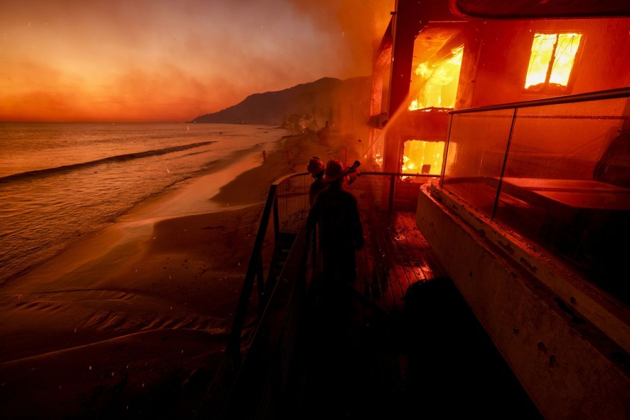 Firefighters work from a deck as the Palisades Fire burns a beachfront property Jan. 8, 2025, in Malibu, Calif. 