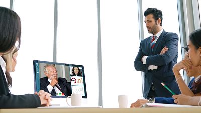 Video call in an office environment, with an older male executive seen smiling on the screen