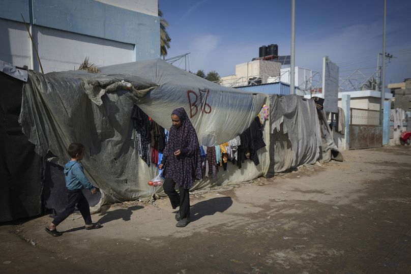 امرأة وطفل يسيران خارج خيمتهما في مخيم للنازحين الفلسطينيين في دير البلح، وسط قطاع غزة، الجمعة 17 يناير، 2025. 